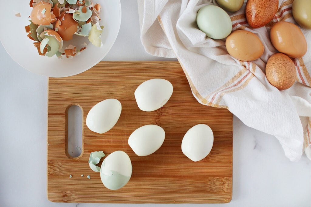 Hard boiled eggs on a wooden cutting board being peeled.
