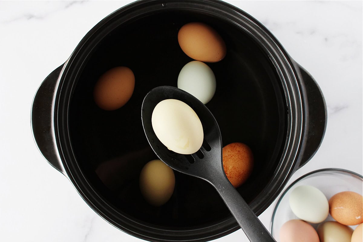A slotted spoon transferring colorful eggs to a pot of boiling water.