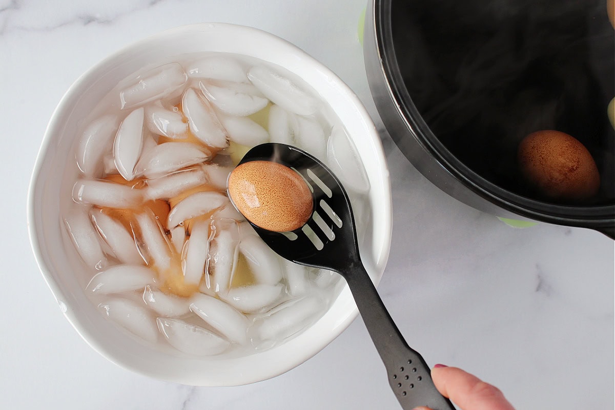 Using a slotted spoon to transfer boiled eggs to a bowl of ice water.