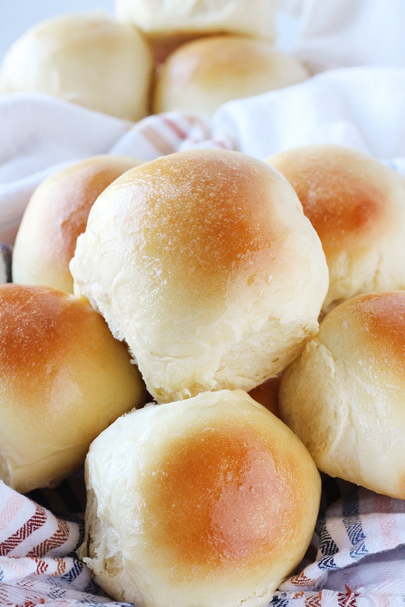 Homemade sourdough rolls stacked in a towel lined basket.