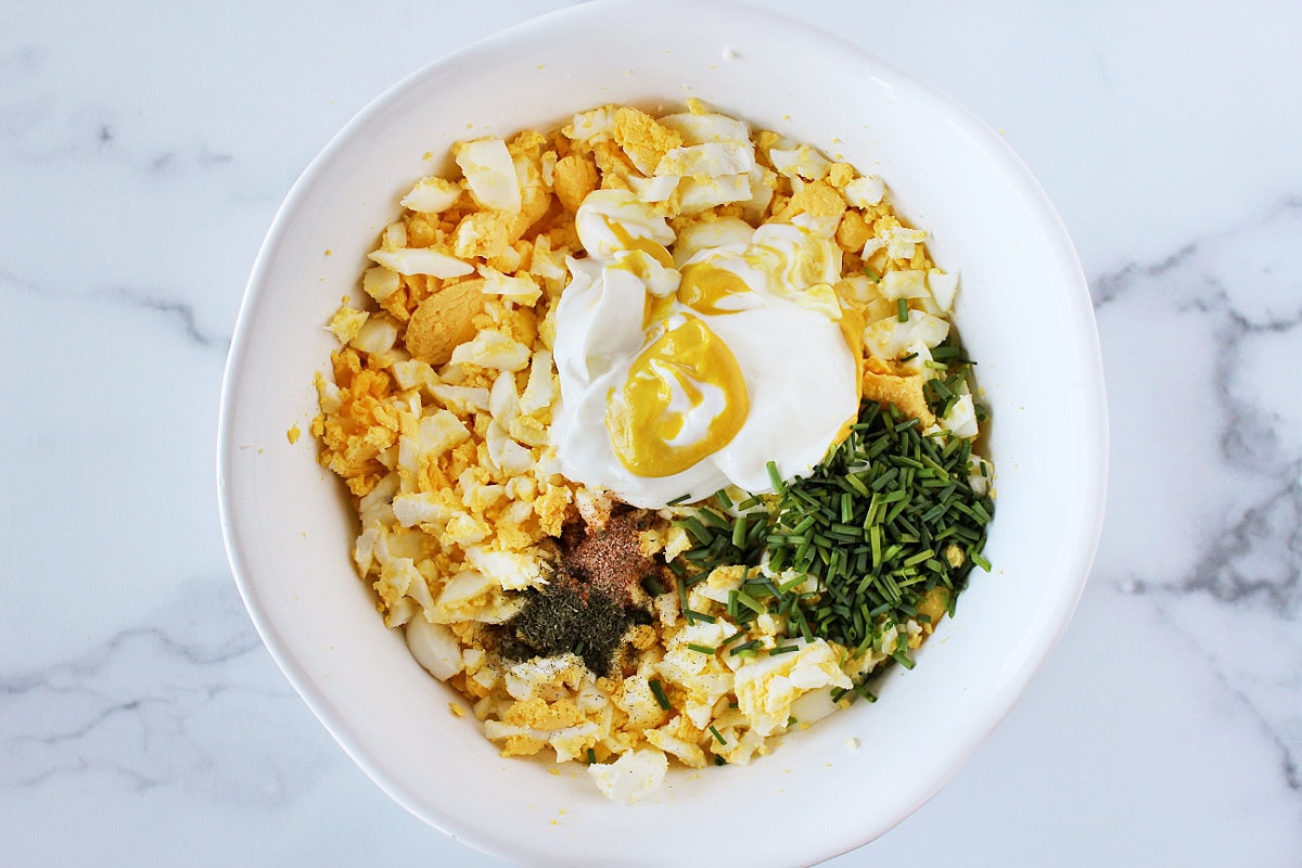 Chopped hard boiled eggs, plain Greek yogurt, mustard, and seasonings in a bowl.