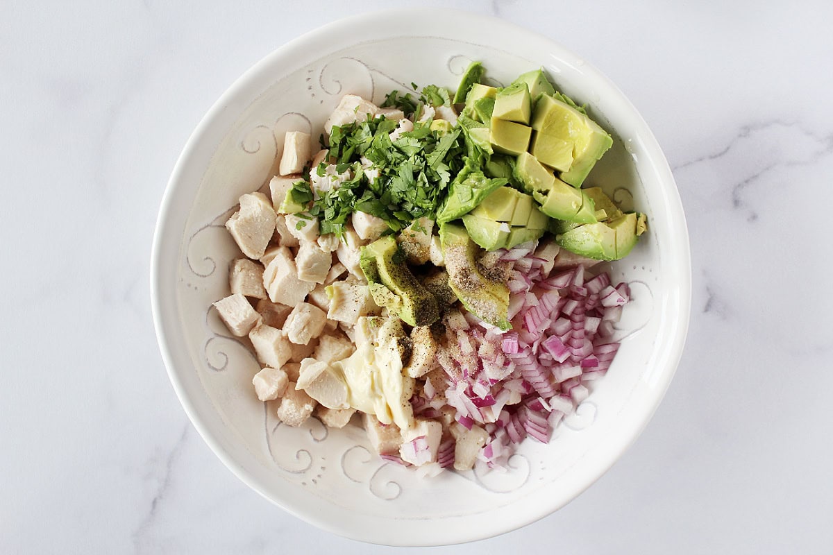 Mayo, diced chicken, avocado, cilantro, and red onion in a white mixing bowl.