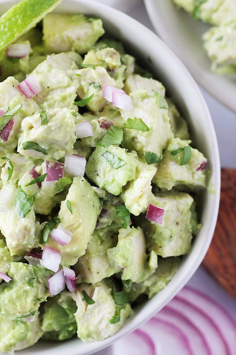 Cilantro, red onion, and lime wedges on top of chicken avocado salad.