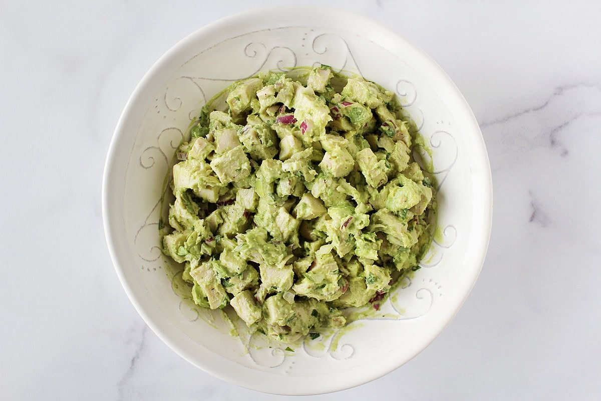 Avocado chicken salad with red onion, mayo, and cilantro mixed in a bowl.