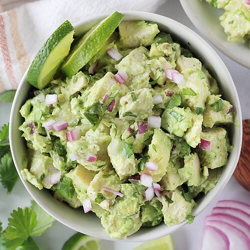 Diced red onion and cilantro on top of avocado chicken salad in a bowl.