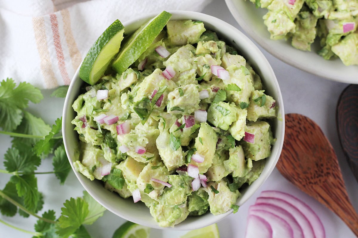 Diced red onion and cilantro on top of avocado chicken salad in a bowl.