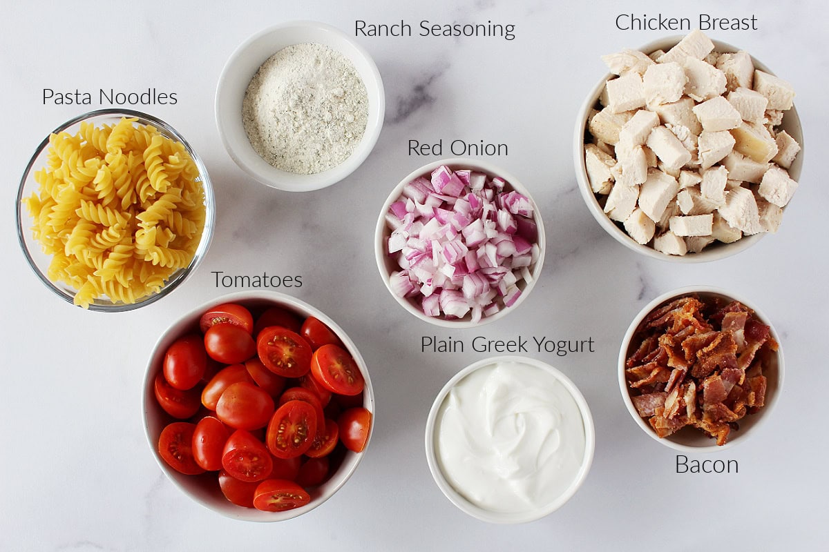 Labeled ingredients for chicken bacon ranch pasta salad on a white marble countertop.