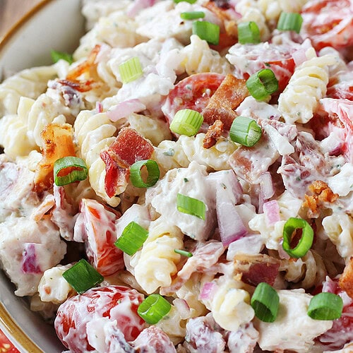 Cooked bacon and green onions on chicken ranch pasta salad in a bowl.