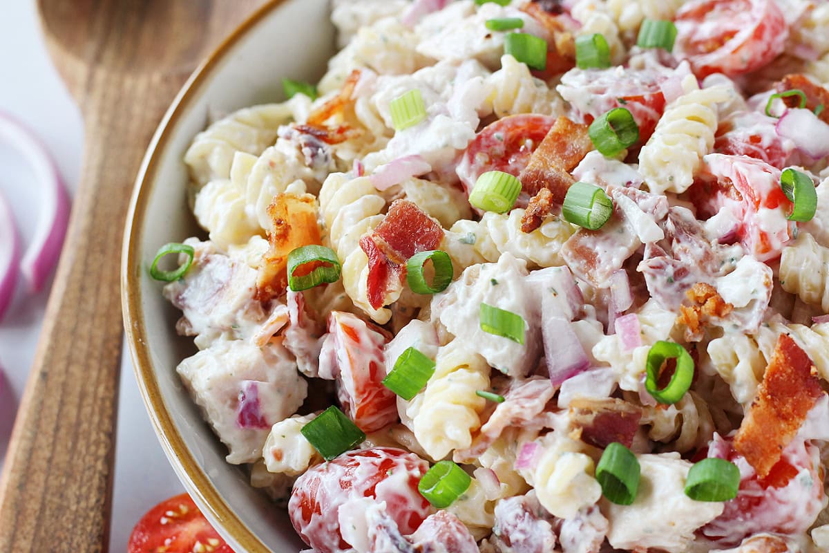 Cooked bacon and green onions on chicken ranch pasta salad in a bowl.