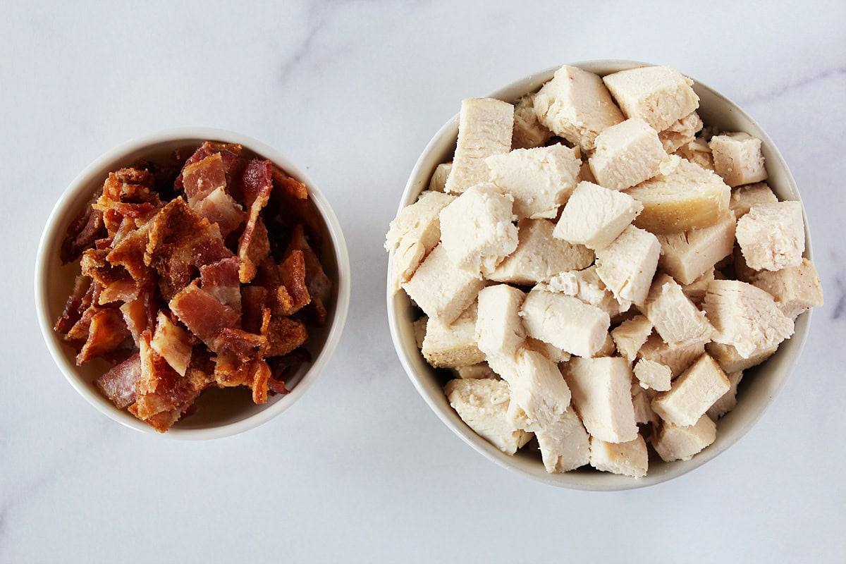 Chopped cooked bacon and diced chicken breast in ceramic bowls.