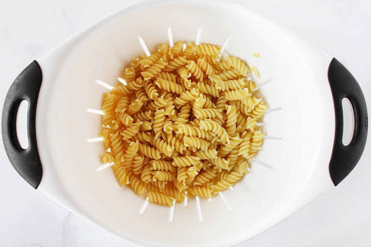 Cooked rotini pasta in a white colander.