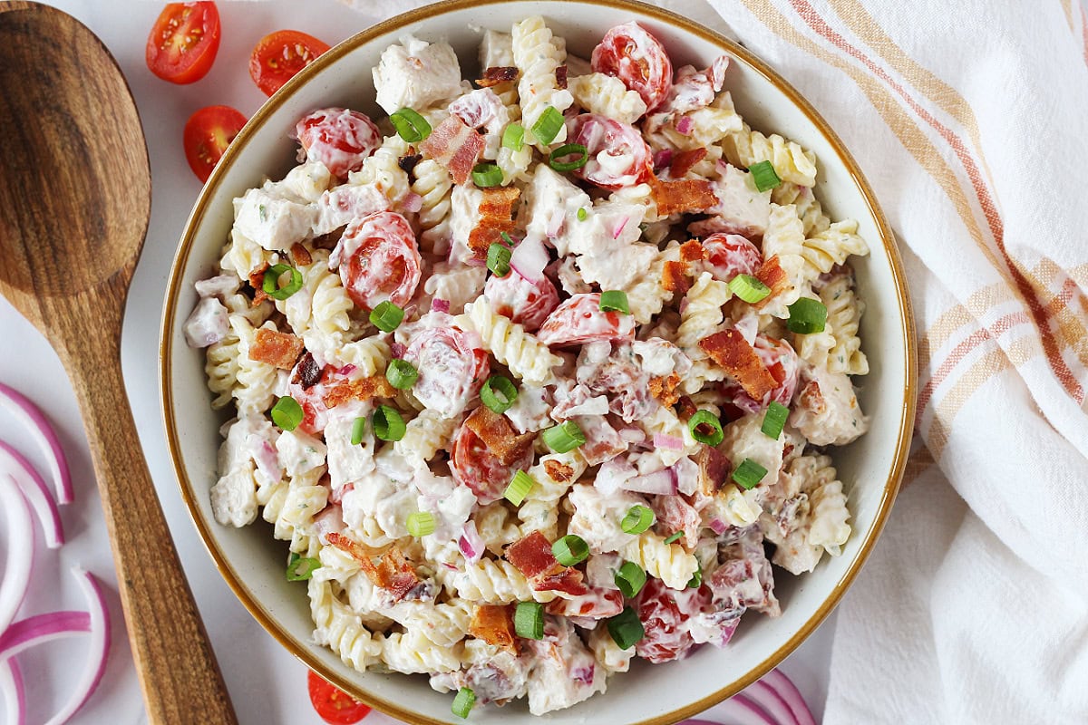Chicken bacon ranch pasta salad in a white bowl with a wooden spoon on the side.