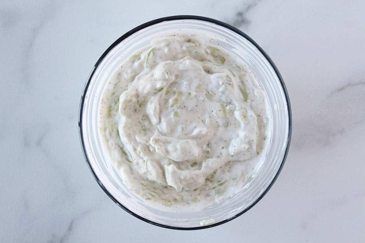 Tzatziki in a glass bowl on a white marble countertop.