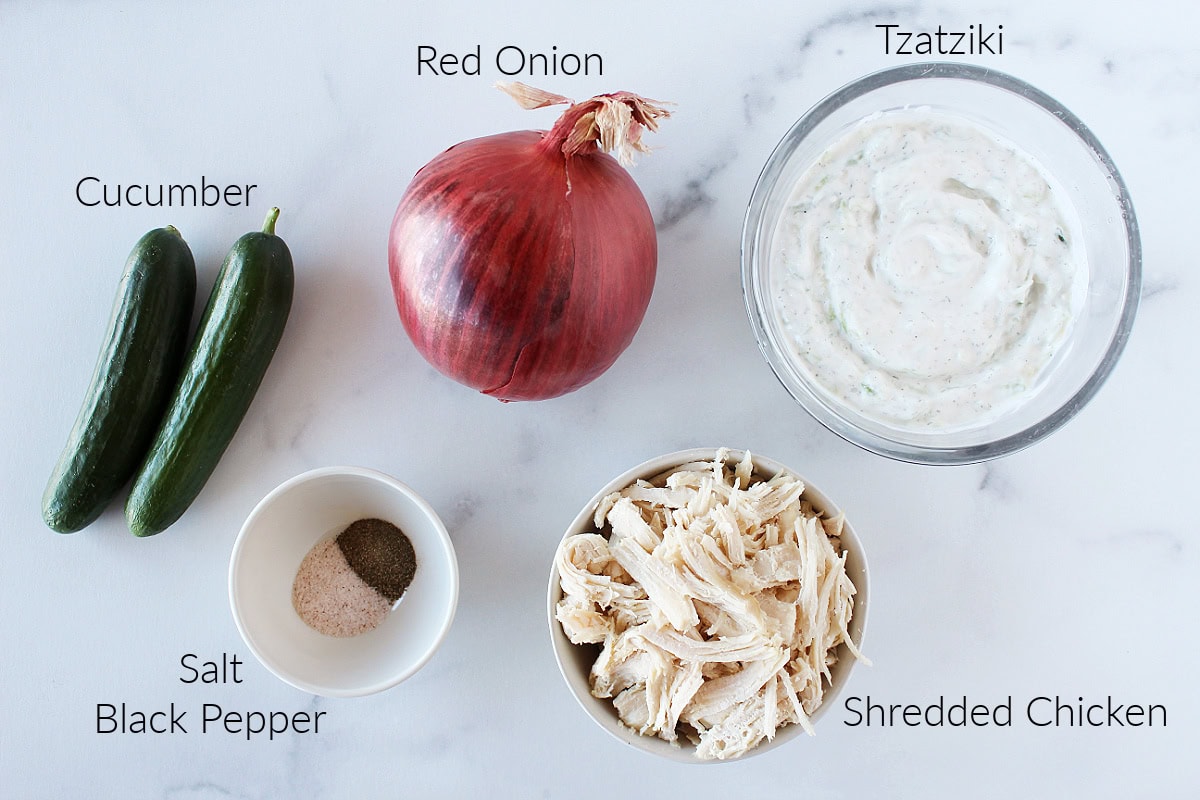 Labeled ingredients for tzatziki chicken salad on a white marble countertop.