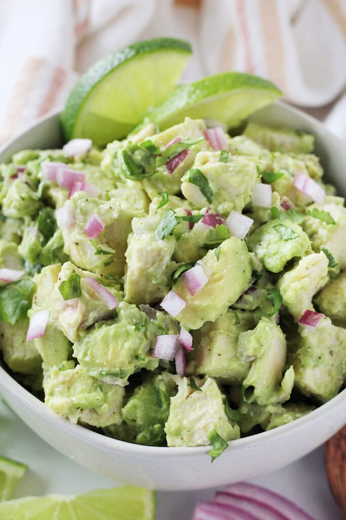 Creamy avocado chicken salad in a white bowl with lime slices and red onion.