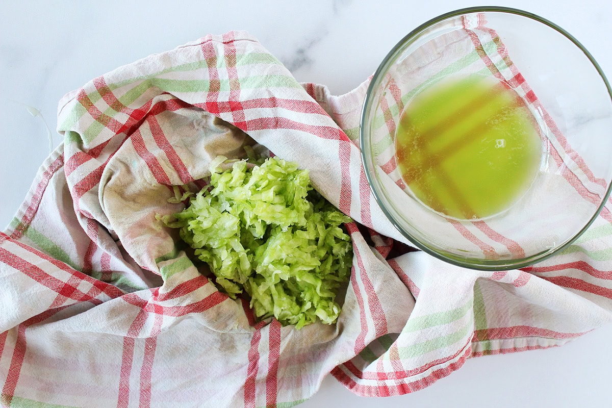 Shredded cucumber on a kitchen towel with the cucumber juice in a glass bowl.