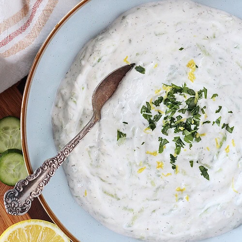 Homemade tzatziki in a blue ceramic bowl with a spoon.