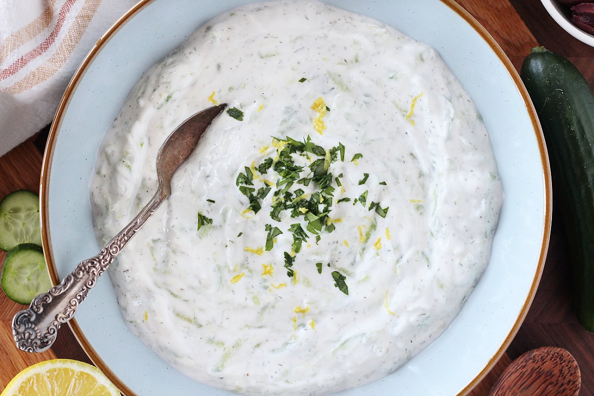 Homemade tzatziki in a blue ceramic bowl with a spoon.