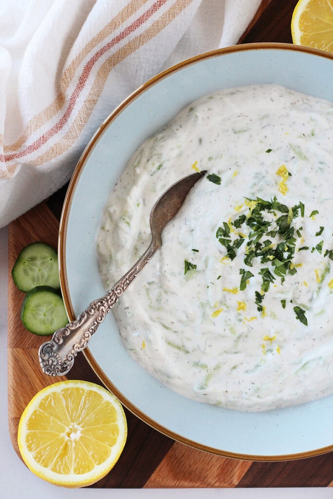 A spoon in a bowl of homemade tzatziki topped with fresh parsley.