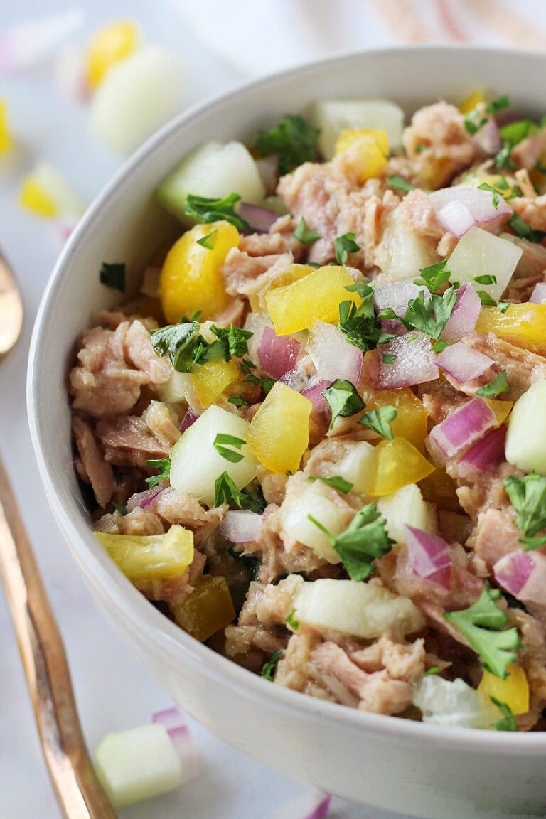 Cucumber, bell pepper, and red onion mixed with canned tuna in a bowl.