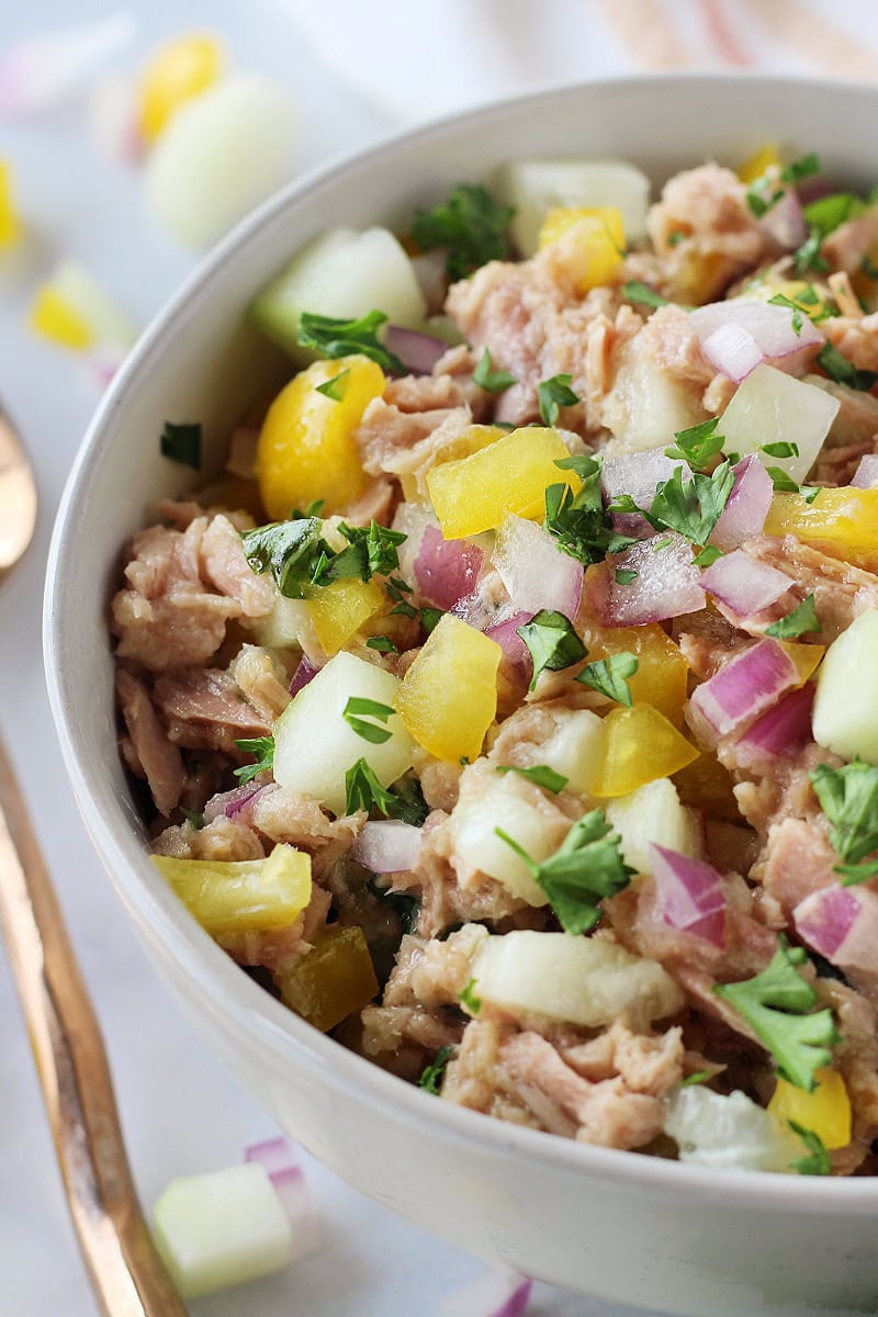 Cucumber, bell pepper, and red onion mixed with canned tuna in a bowl.
