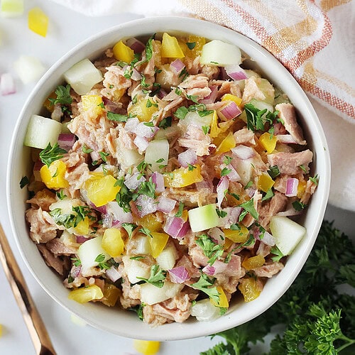 Fresh veggies and herbs in tuna salad in a white bowl.