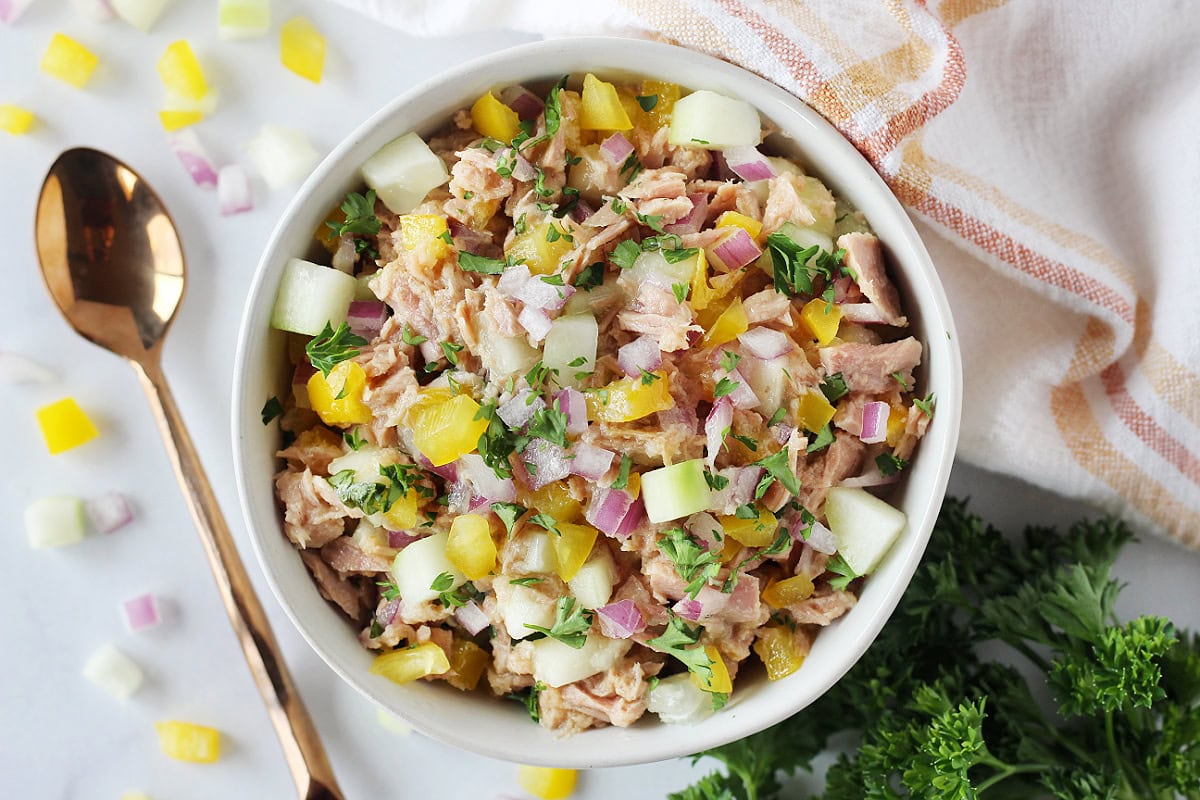 Fresh veggies and herbs in tuna salad in a white bowl.