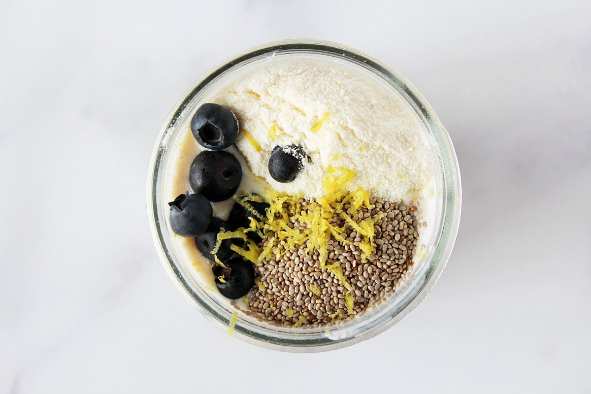 Blueberries, lemon zest, pudding mix, and chia seeds on milk and oats in a jar.