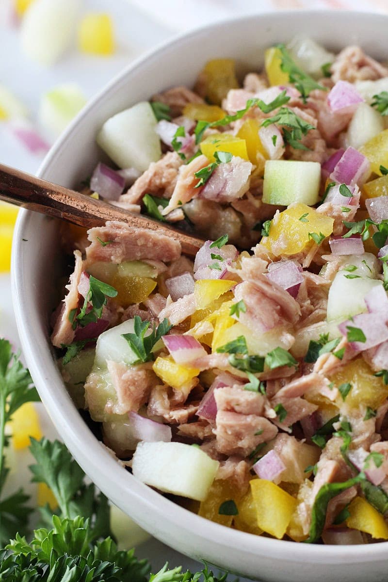 A copper spoon in a bowl of colorful Mediterranean Tuna Salad with veggies.