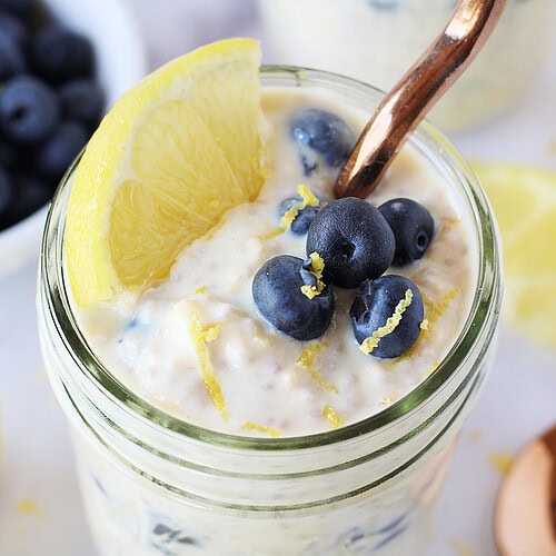Lemon wedge and zest topping blueberry overnight oats in a mason jar with spoon.