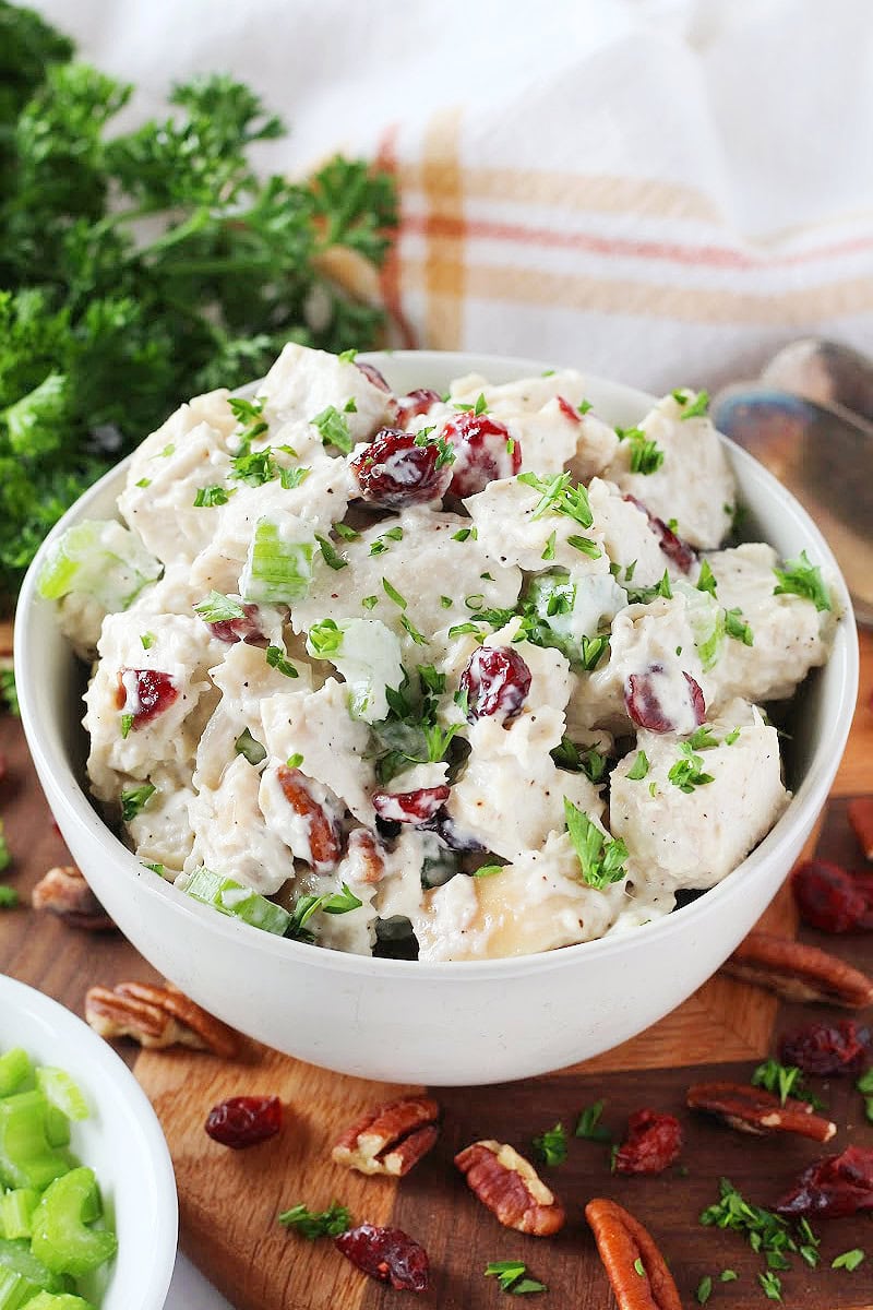Creamy pecan cranberry chicken salad in a white bowl topped with chopped parsley.