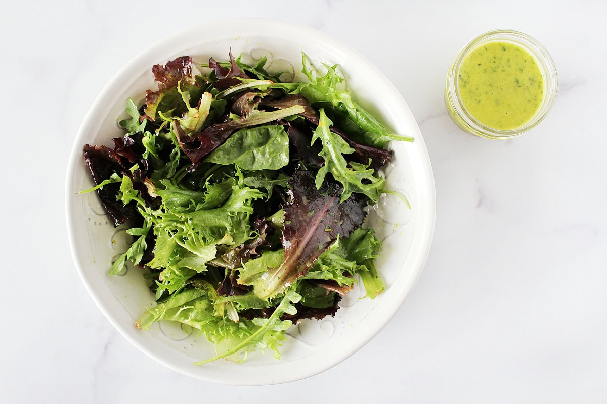 Citrus dressing in a mason jar next to bowl of mixed greens.