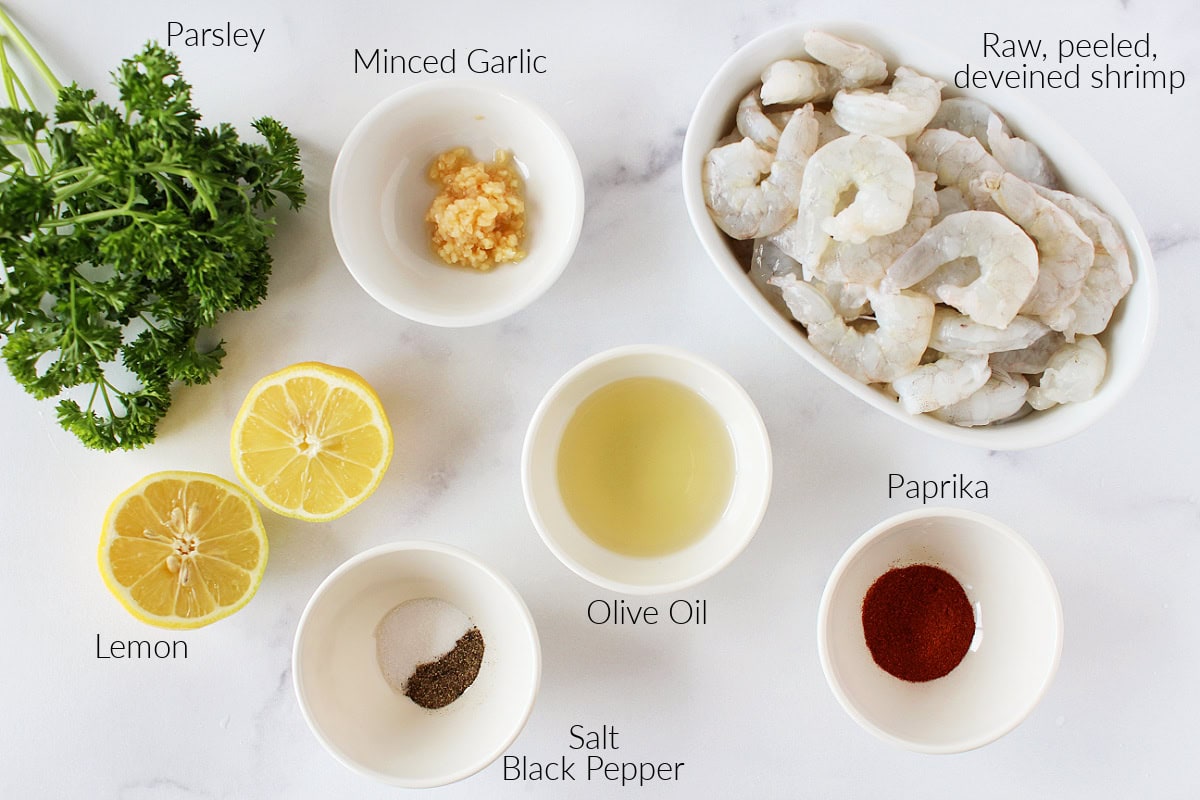 Labeled ingredients for oven baked shrimp on a white marble countertop.