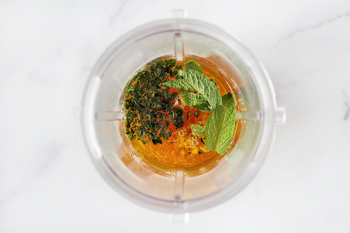 Mint leaves and chopped basil on orange juice and olive oil in blender jar.