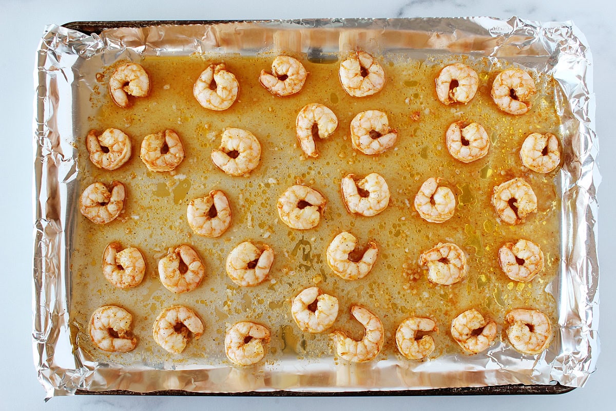 Oven baked shrimp on a foil lined baking sheet.