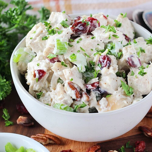 Chopped parsley garnishing cranberry pecan chicken salad in a white bowl.