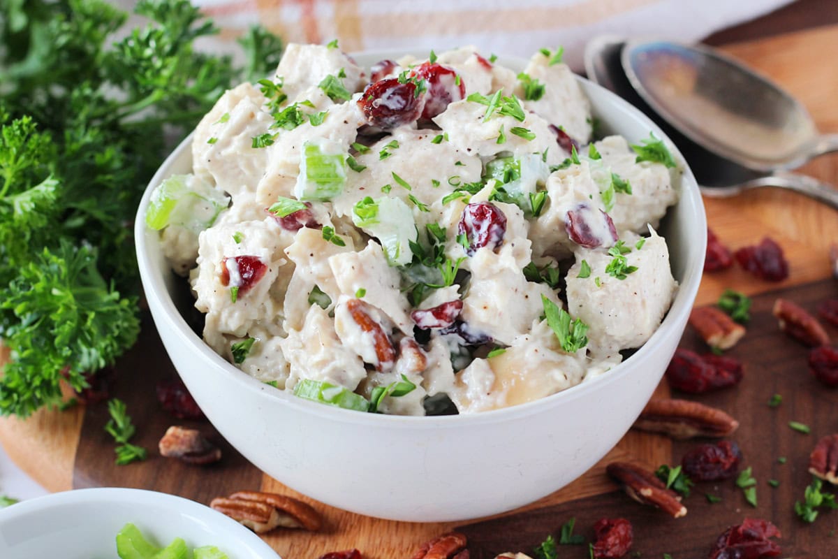 Chopped parsley garnishing cranberry pecan chicken salad in a white bowl.