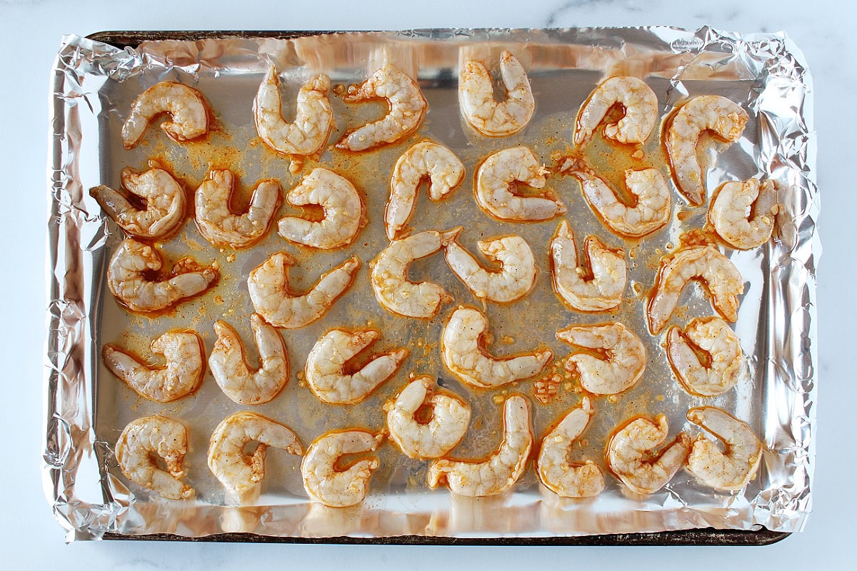 Raw marinated shrimp on an aluminum foil lined baking sheet.