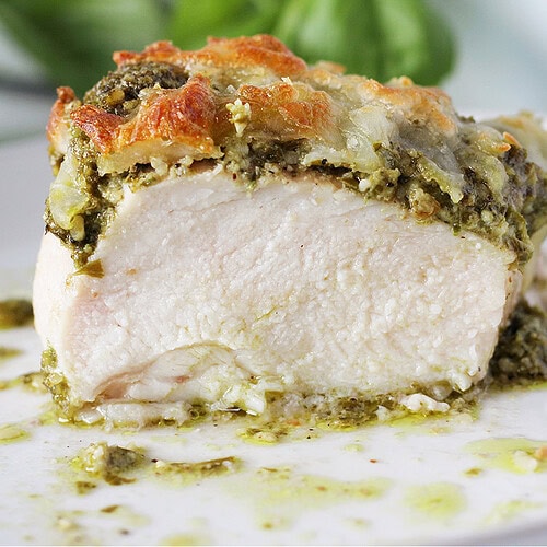 A halved chicken breast topped with homemade basil pesto and mozzarella.