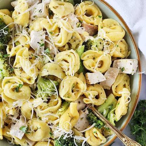 Gold spoon in bowl of cheese tortellini, broccoli, and diced chicken breast.