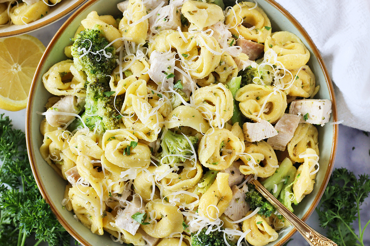 Gold spoon in bowl of cheese tortellini, broccoli, and diced chicken breast.