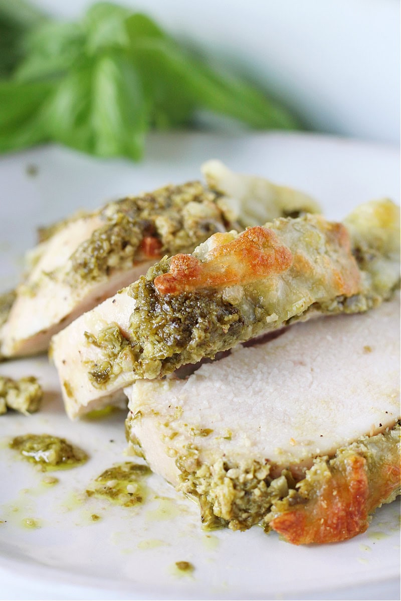 Three slices of baked pesto chicken on a white plate.