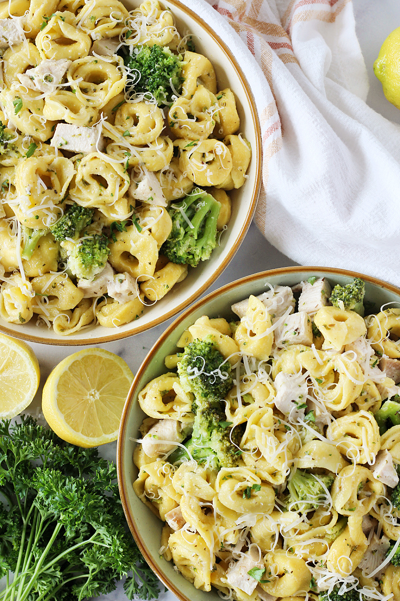 Two bowls of cheese tortellini with broccoli and chicken breast.